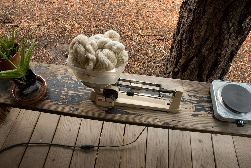 A small pile of wool yarn on a scale, on a bench with a heating element and some aloe vera plants.