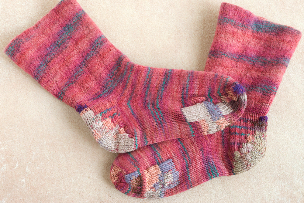 Fuchsia hand-knit socks with many overlapping duplicate-stitch patches in different yarns.